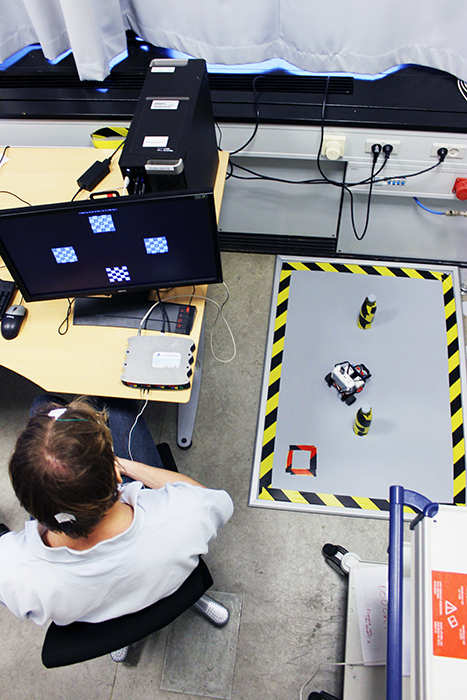 Testperson med 3 elektroder monteret på hovedbunden styrer lille robot igennem en bane på pladen til højre ved at kigge på forskellige felter på en skærm. (Foto: Signe K.D. Engelsholm)